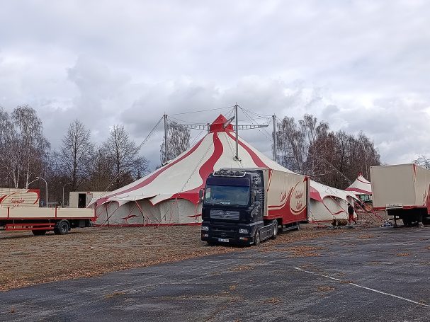 Fertig aufgebautes rot- weißes Zirkuszelt mit Zirkuswagen bei bewölkten Himmel 