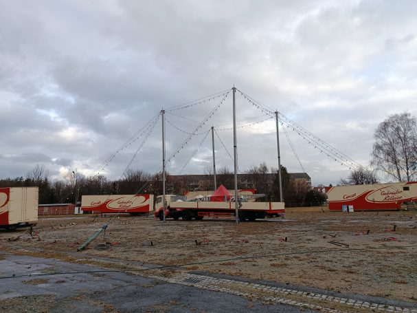 Zeltplatz mit abgebauten Zirkuswagen und Masten unter einem bewölkten Himmel.